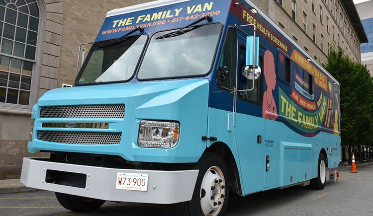 A brightly painted blue mobile clinic van parked on a city street. The side reads “The Family Van” and advertises free health screenings, with the website and phone number displayed above the windshield.