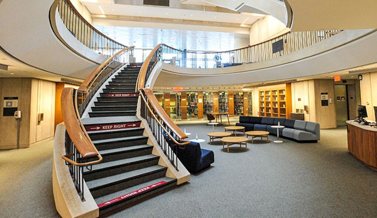 The interior of Countway Library, showing the renovated lower level and a curving staircase leading to upper levels.