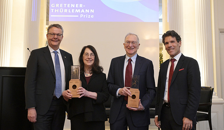 Sharpe and Freeman hold their awards, flanked by Shaepman and Dall'O. They stand in front of a screen with the prize name on it.