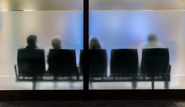 An abstract photograph of a waiting room with frosted glass and people sitting in chairs
