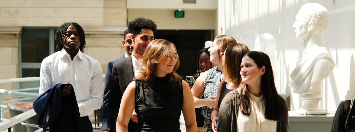 New MD students proudly walking in the medical education building in front of marble busts of historical school figures. 