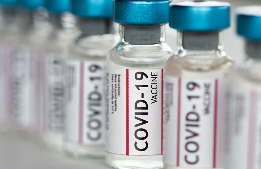 A row of vials labeled COVID-19 vaccine sits on a shelf.