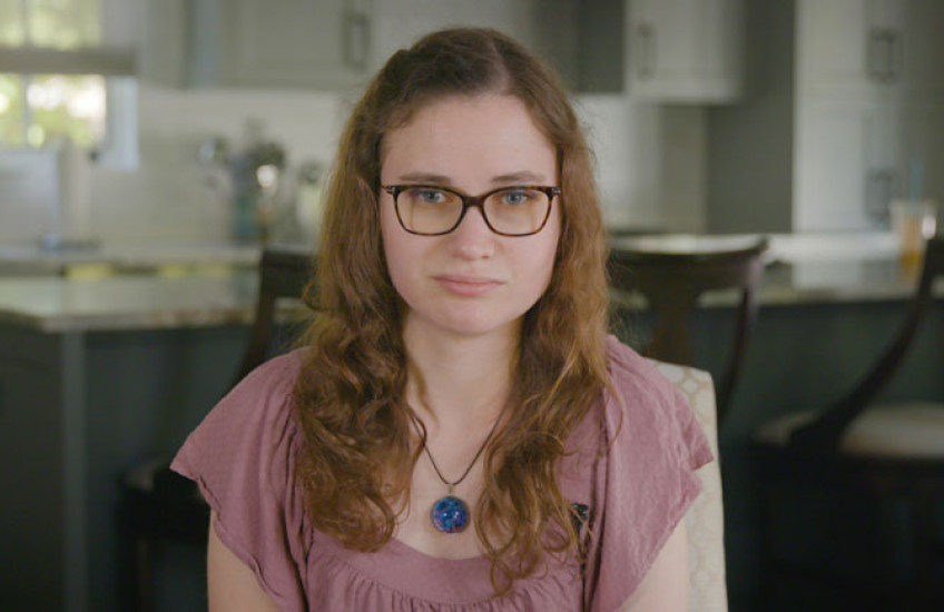 A shot of Jessica Chaikof from the chest up, wearing a pink shirt and glasses