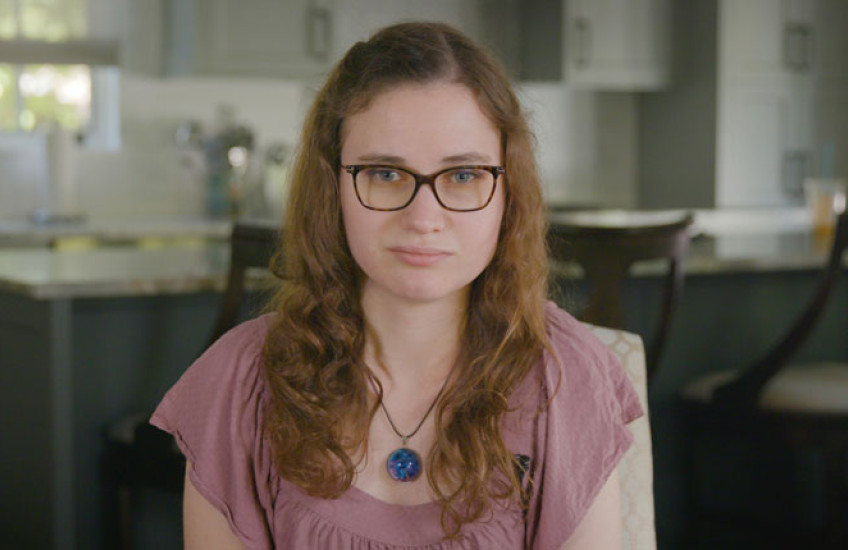 A shot of Jessica Chaikof from the chest up, wearing a pink shirt and glasses