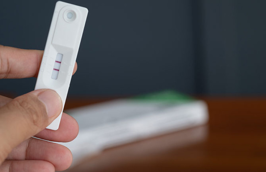 A person holds an at-home COVID test displaying two dark red lines