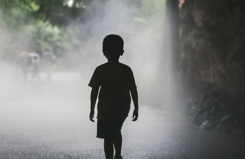 Silhouette of a young boy walking alone on a foggy, tree-lined path