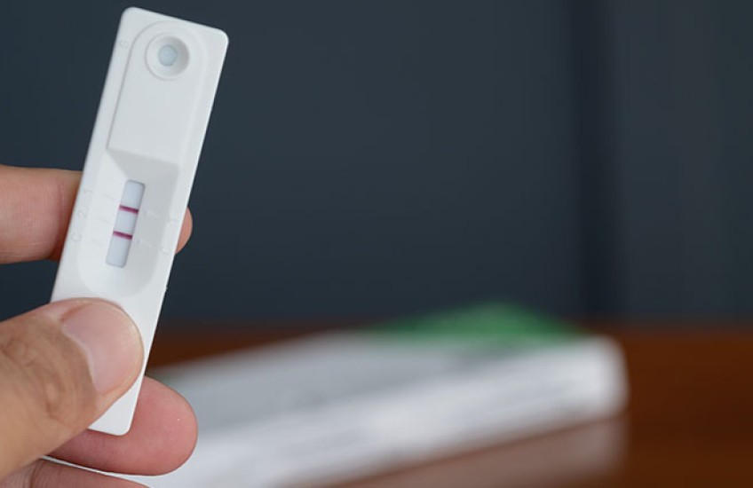 A person holds an at-home COVID test displaying two dark red lines