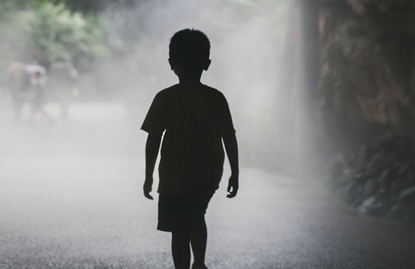 Silhouette of a young boy walking alone on a foggy, tree-lined path