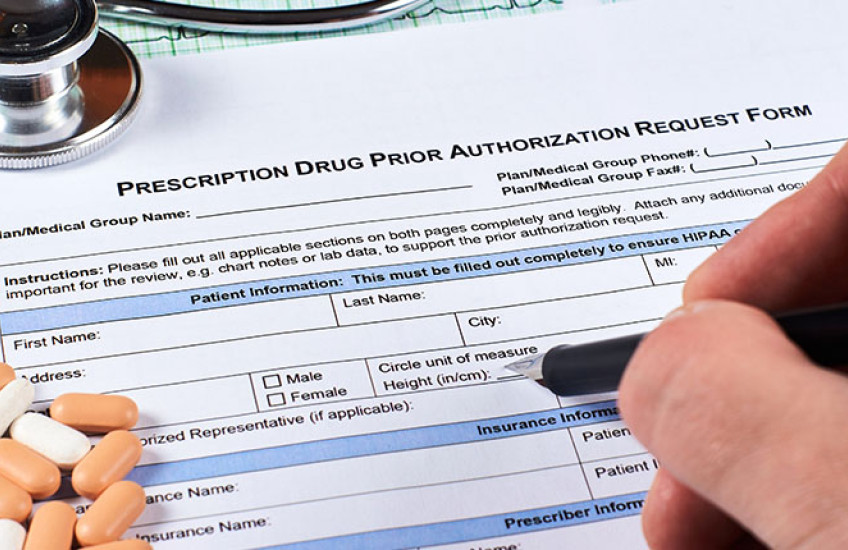 Photo of hand filling out a form, labeled "Prescription Drug Prior Authorization Form."