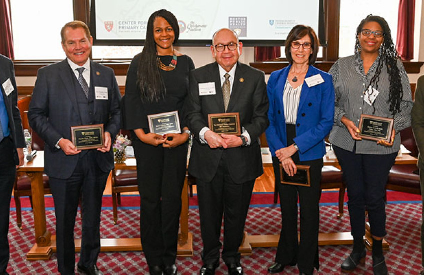 Seven panelists in a line, facing the camera and holding commemorative plaques