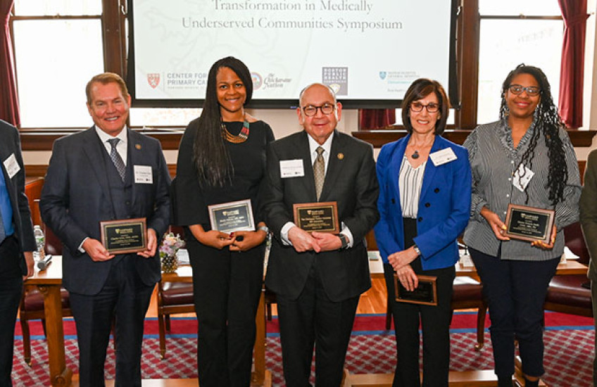 Seven panelists in a line, facing the camera, holding commemorative plaques