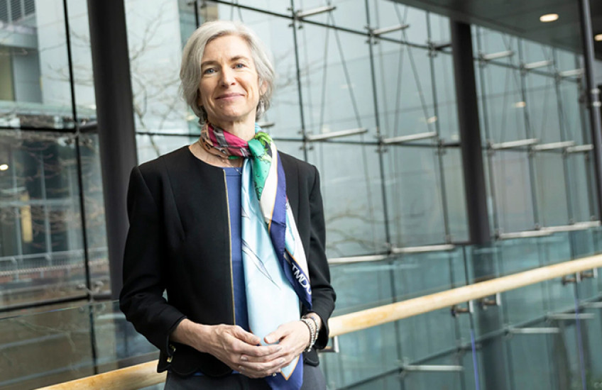 portrait photo of Jennifer Doudna, a slightly smiling white woman with chin-length gray hair, leaning against a railing in front of a wall of windows. she wears a blazer and colorful silk scarf