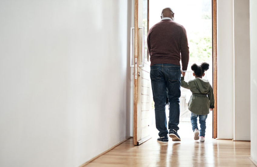 Man holding hand of small child walking through a doorway from inside to outside