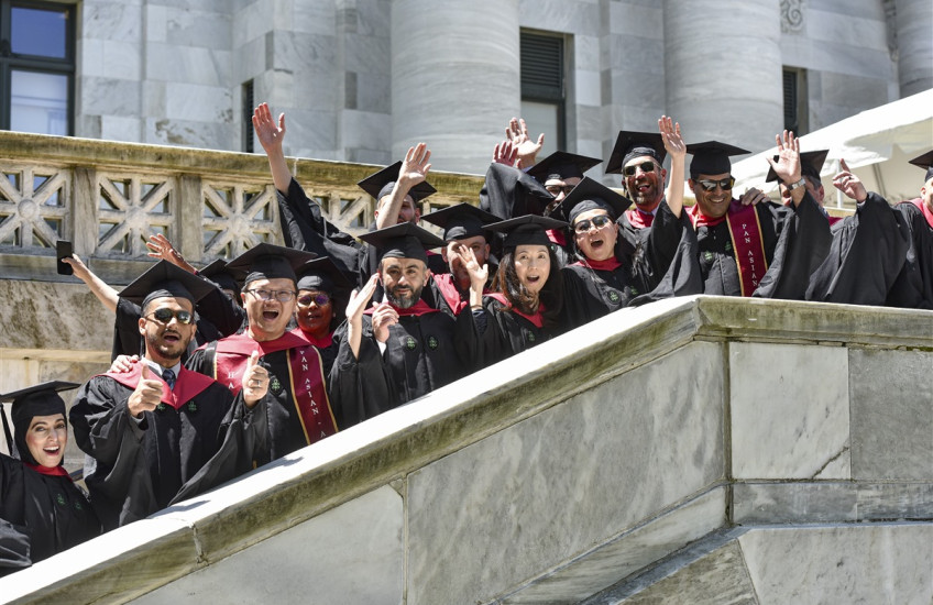 More than a dozen graduates in regalia cheer on the marble stairway at one side of HMS's Gordon Hall