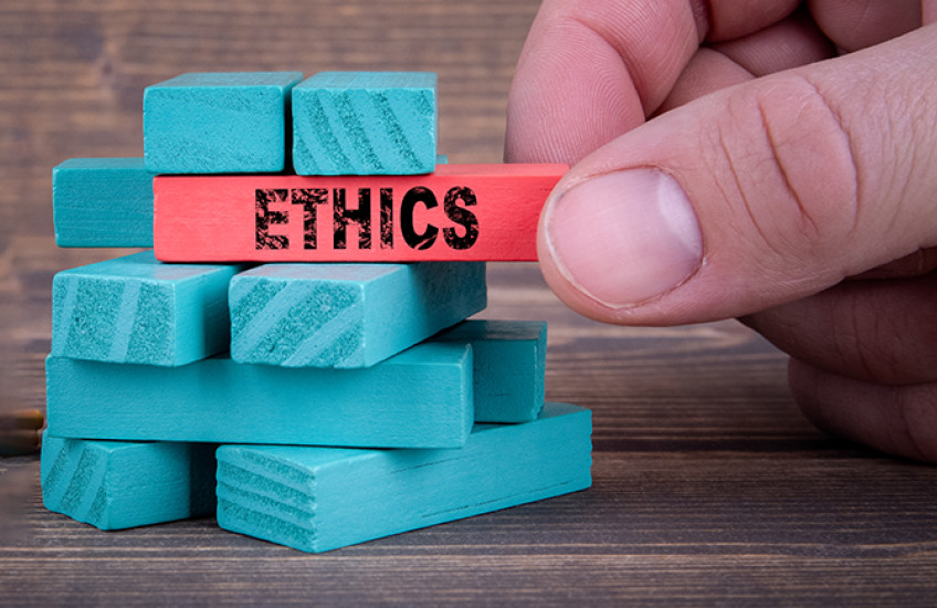 An unseen person holds a Jenga-style block labeled "Ethics" within a stack of similar blocks