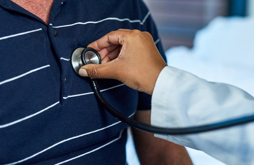 Close-up photo of the arm of a clinician of color holding a stethoscope to a patient's chest
