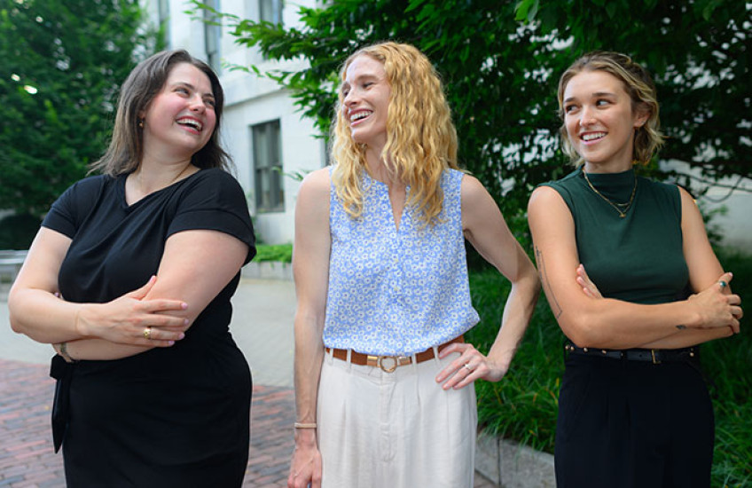 Three young women stand in courtyard smiling at each other