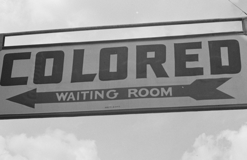 A sign pointing the way to the “colored waiting room” in a 1943 photo of a scene from Rome, Georgia, symbolizes how a legacy of historic racism leads to unequal health care for Black people, Native Americans, and members of other groups that still face discrimination today.