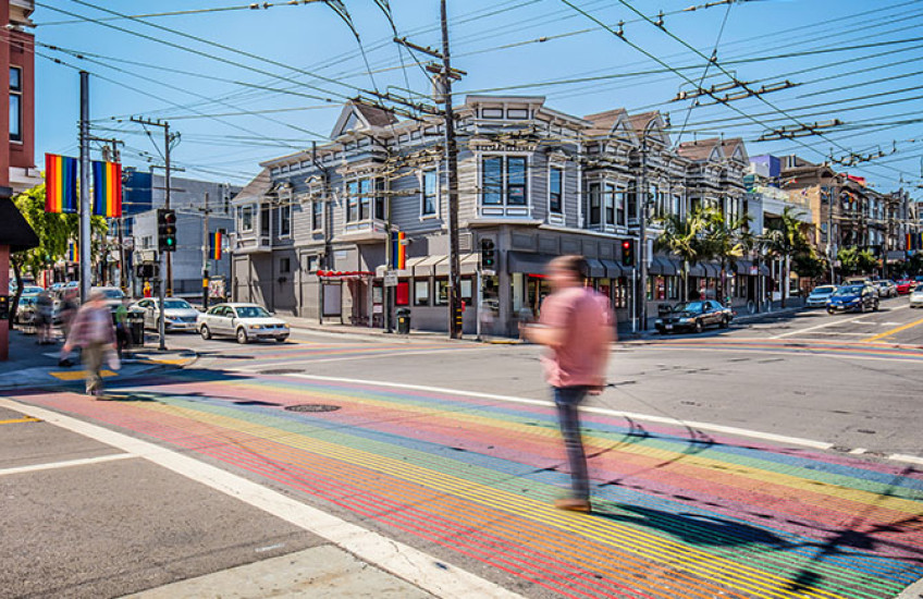 People in colorful outfits cross the street at an intersection with rainbow crosswalks in San Francisco’s Castro district.