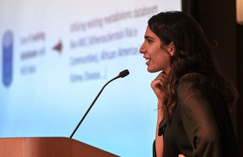 Side view of a young woman presenting at a lectern in front of a projected slide show