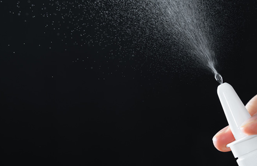 A closeup of a nasal spray nozzle releasing mist into the air