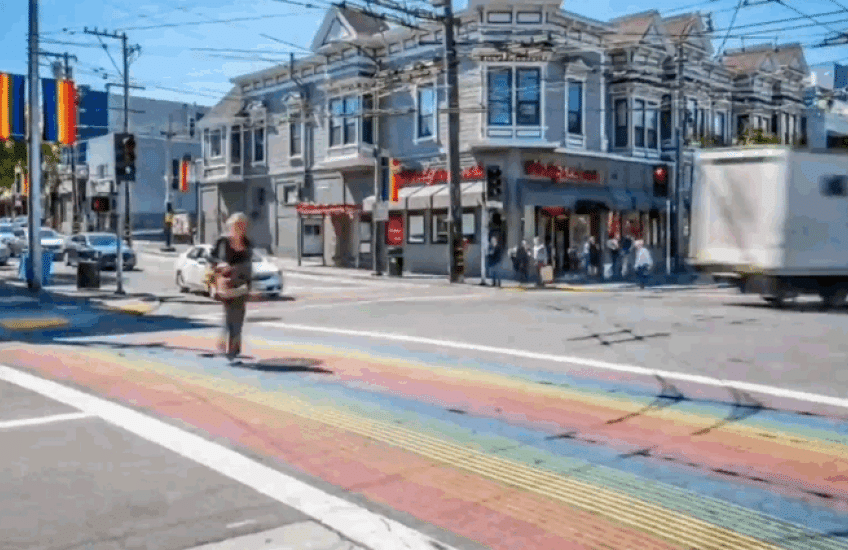 People in colorful outfits cross the street at an intersection with rainbow crosswalks in San Francisco’s Castro district.