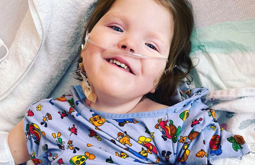 Photo of a young girl lying on blankets wearing a hospital gown featuring cartoon characters.