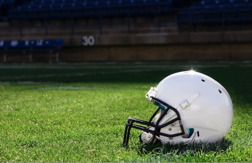 A white football helmet rests on a grass field in a stadium