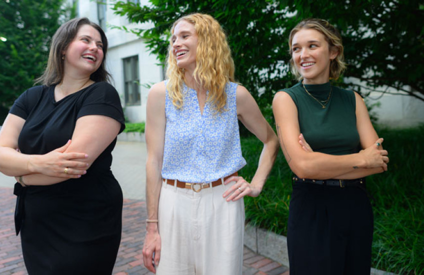 Three young women stand in courtyard smiling at each other