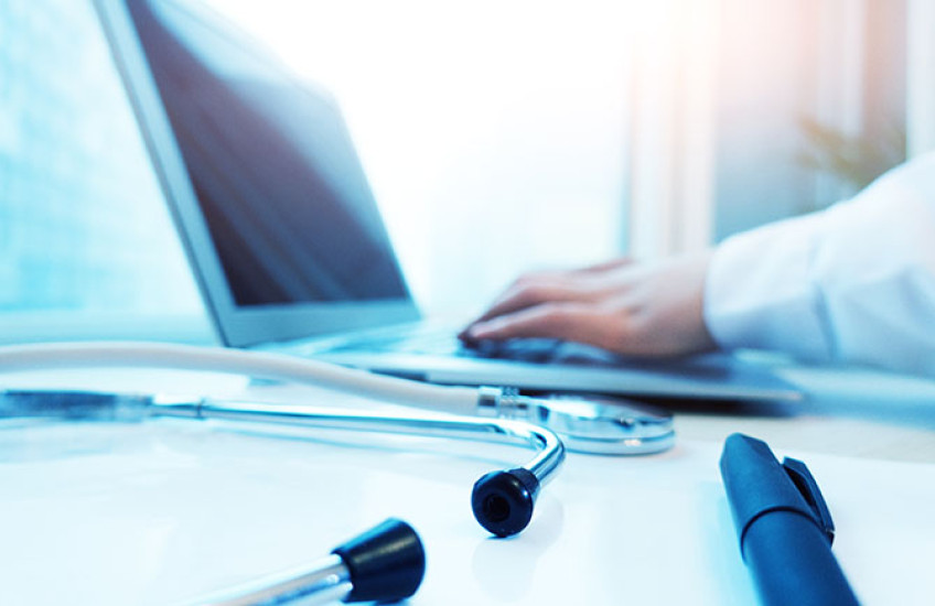 Close-up of a laptop, stethoscope, and physician’s forearm in white coat