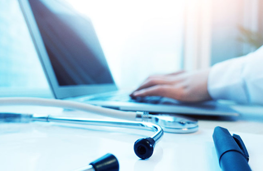 Close-up of a laptop, stethoscope, and physician’s forearm in white coat