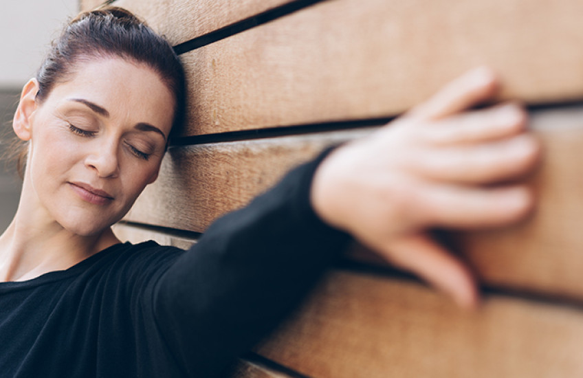 a woman with eyes closed leans her head and her outstretched hand on a wall