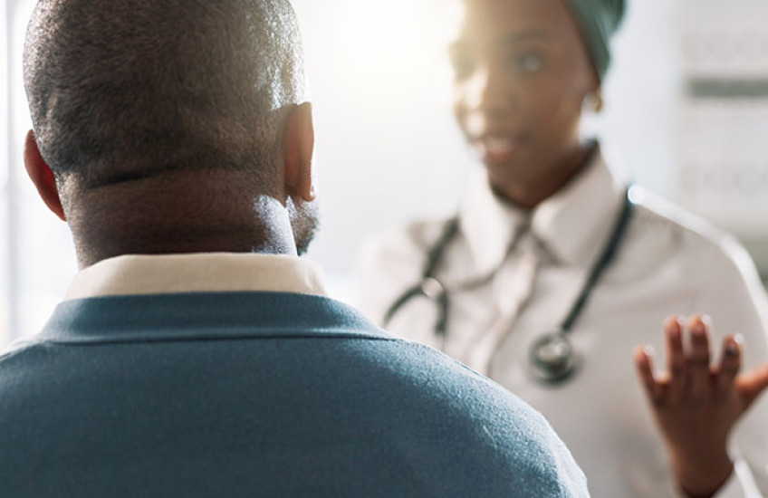 A photograph of a doctor (with face out of focus) talking with her patient, who has his back to the camera.