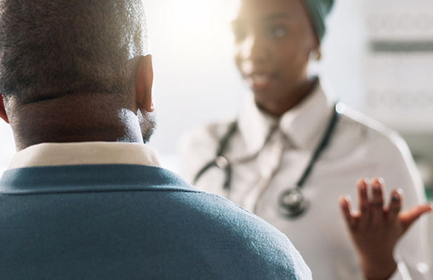 A photograph of a doctor (with face out of focus) talking with her patient, who has his back to the camera.