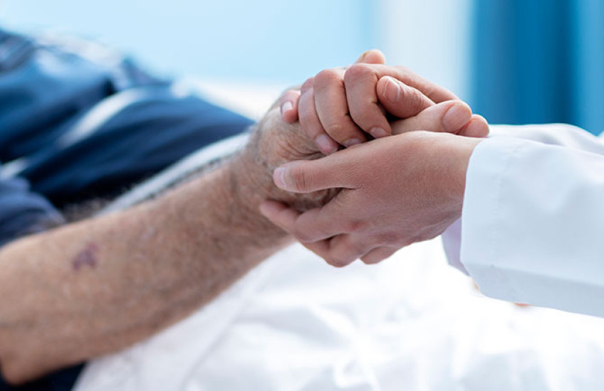 Close up of doctor in white coat holding the hand of an elderly patient