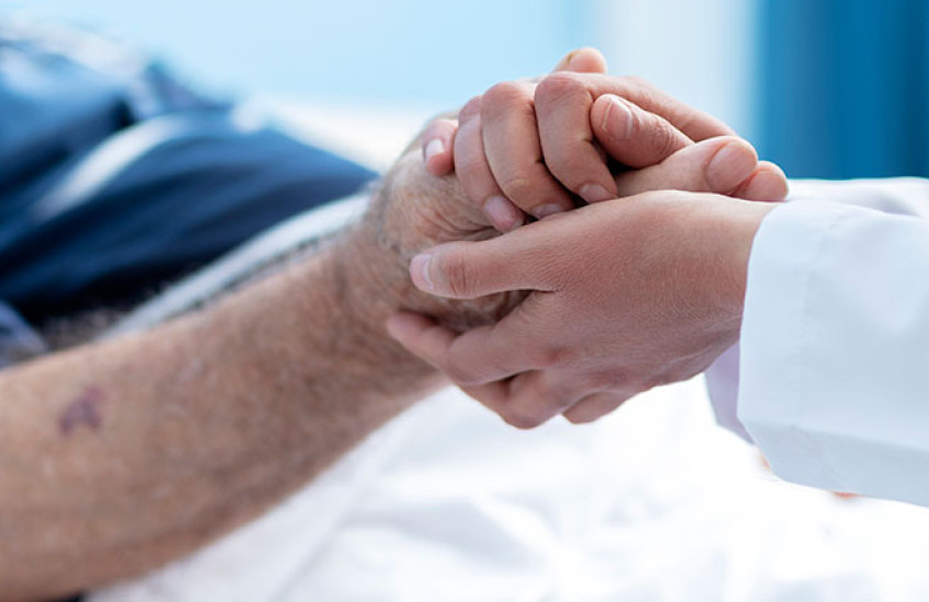 Close up of doctor in white coat holding the hand of an elderly patient