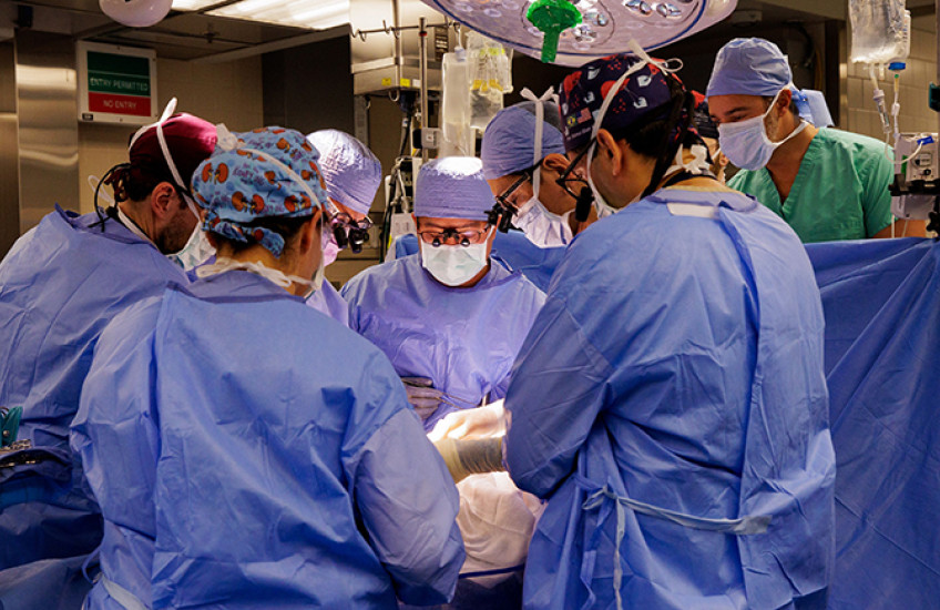 Eight people in surgical garb cluster around an operating table