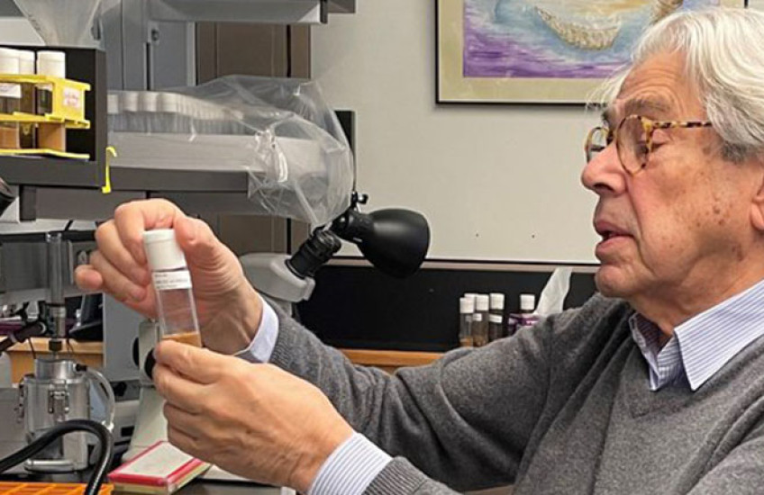 A professor sitting at a lab bench looking at a small plastic container