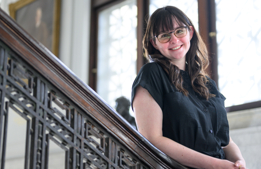 A woman leans on a banister and smiles at the camera