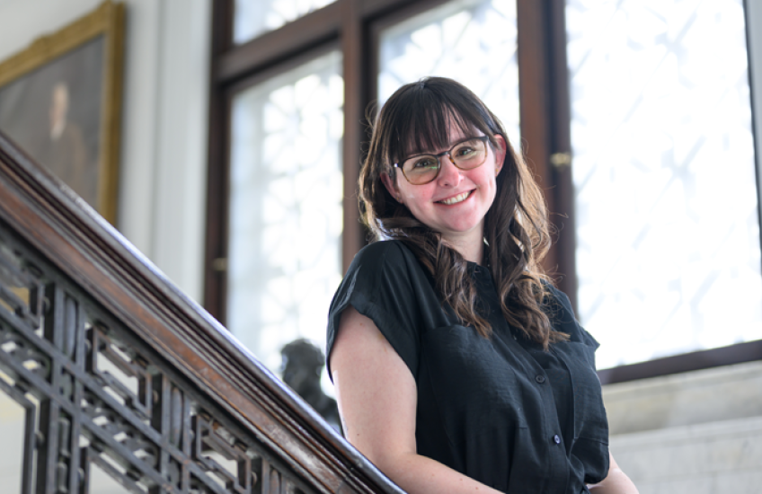 A woman leans on a banister and smiles at the camera