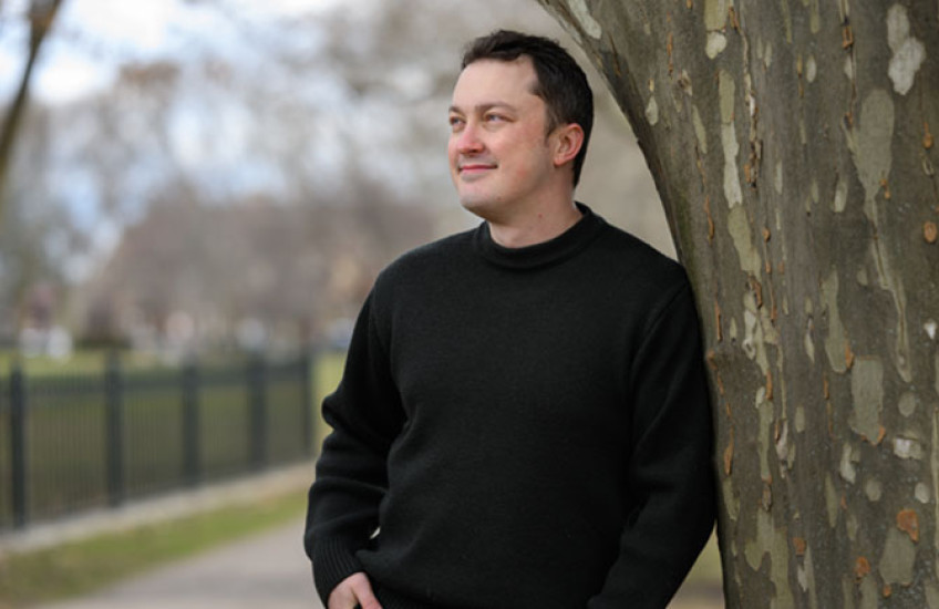 A man leans against a tree, smiling and looking off into the distance
