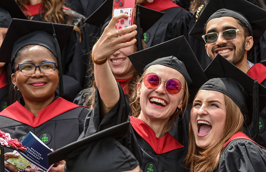 A woman holds up a cell phone to take a selfie with several other people.