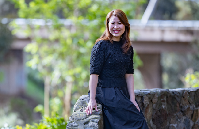 A woman sits on a stone wall and smiles at the camera