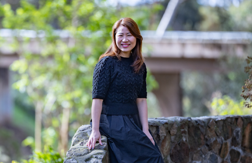 A woman sits on a stone wall and smiles at the camera