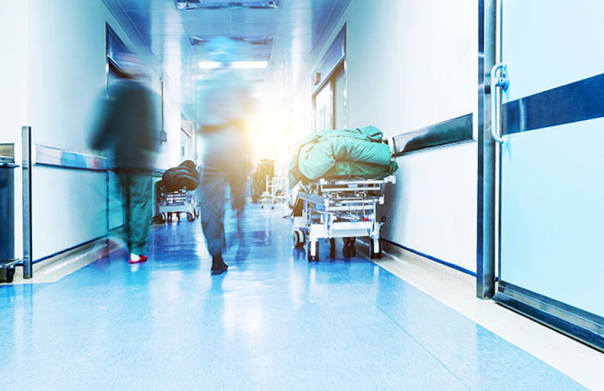 A backlit photo showing health care providers walking up a hallway away from the camera. The unsettling lighting and motion blur convey a sense of unease.