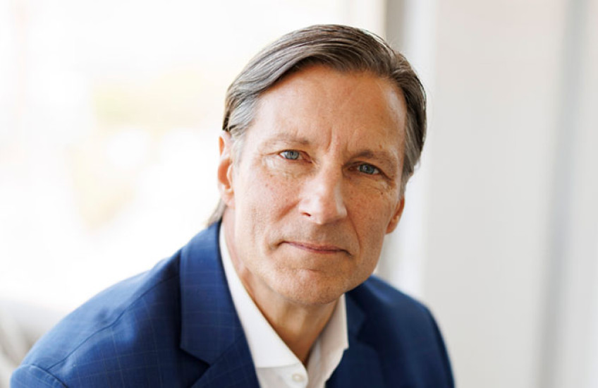 A headshot of a man in a white shirt and blue jacket