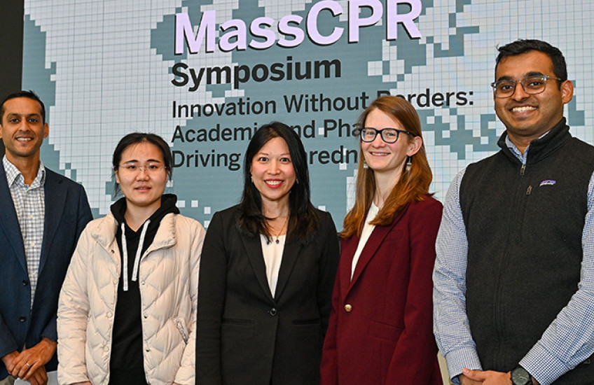 Five people in business clothes pose for a photo in front of a screen with the MassCPR symposium name