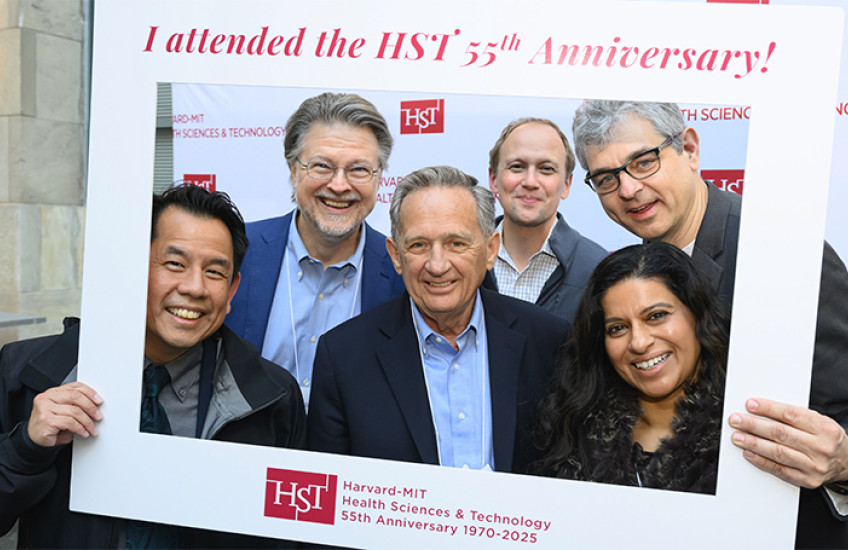 Six people pose, smiling, inside a large portable photo frame that says “Harvard-MIT Health Sciences & Technology 55th Anniversary 1970-2025”