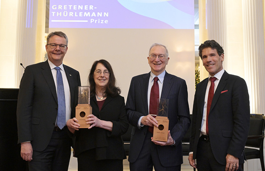 Sharpe and Freeman hold their awards, flanked by Shaepman and Dall'O. They stand in front of a screen with the prize name on it.
