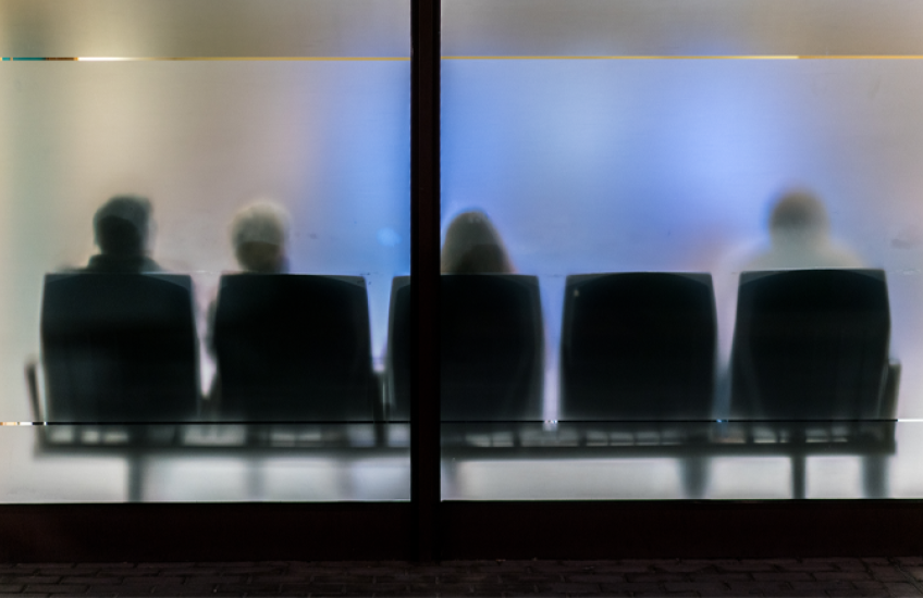 An abstract photograph of a waiting room with frosted glass and people sitting in chairs